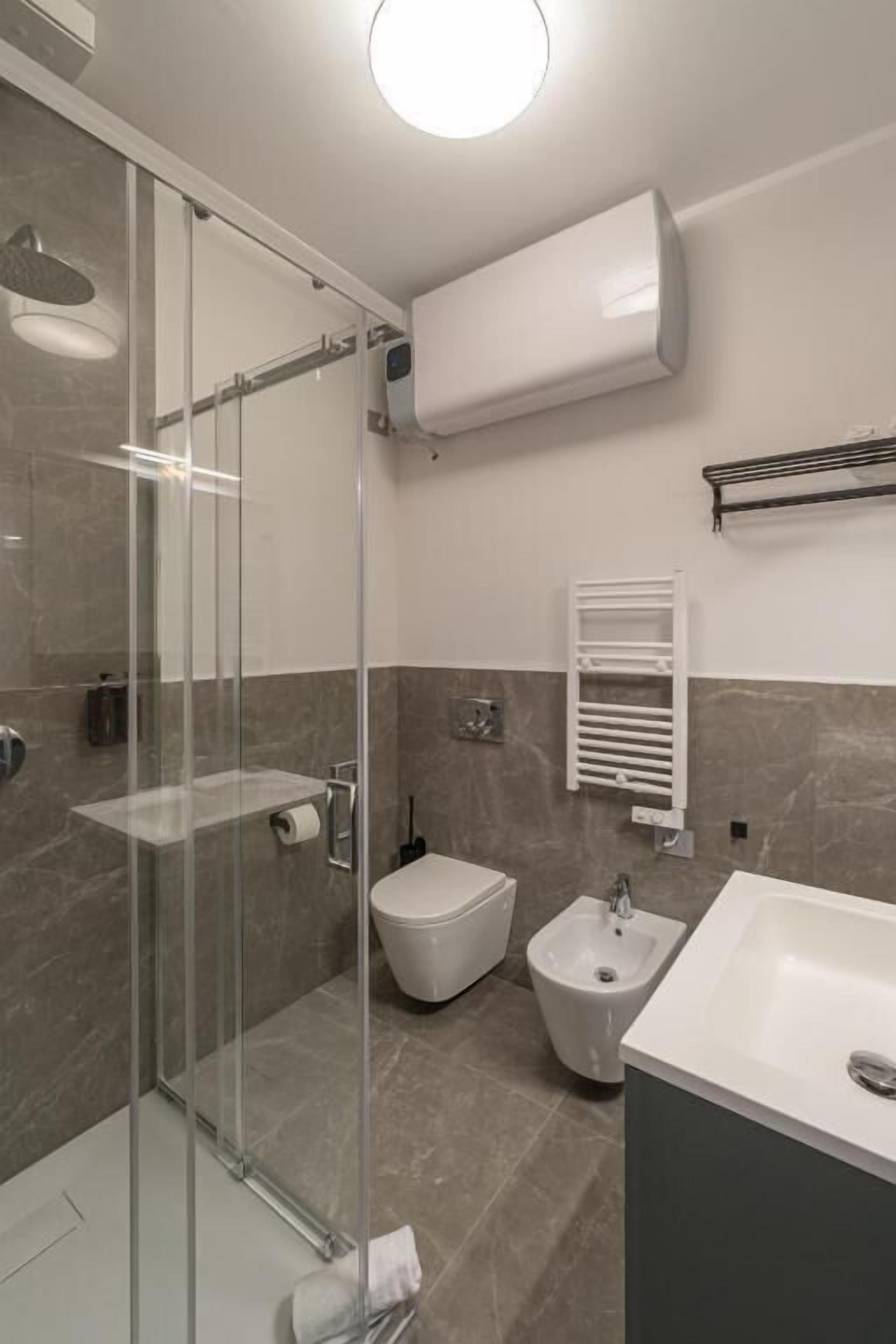 Un bagno moderno con cabina doccia in vetro, un bidet, un lavandino e un porta asciugamani.