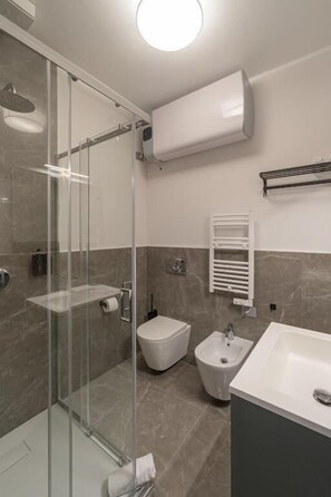 Un baño moderno con cabina de ducha de vidrio, un bidé, un lavamanos y un perchero para toallas.