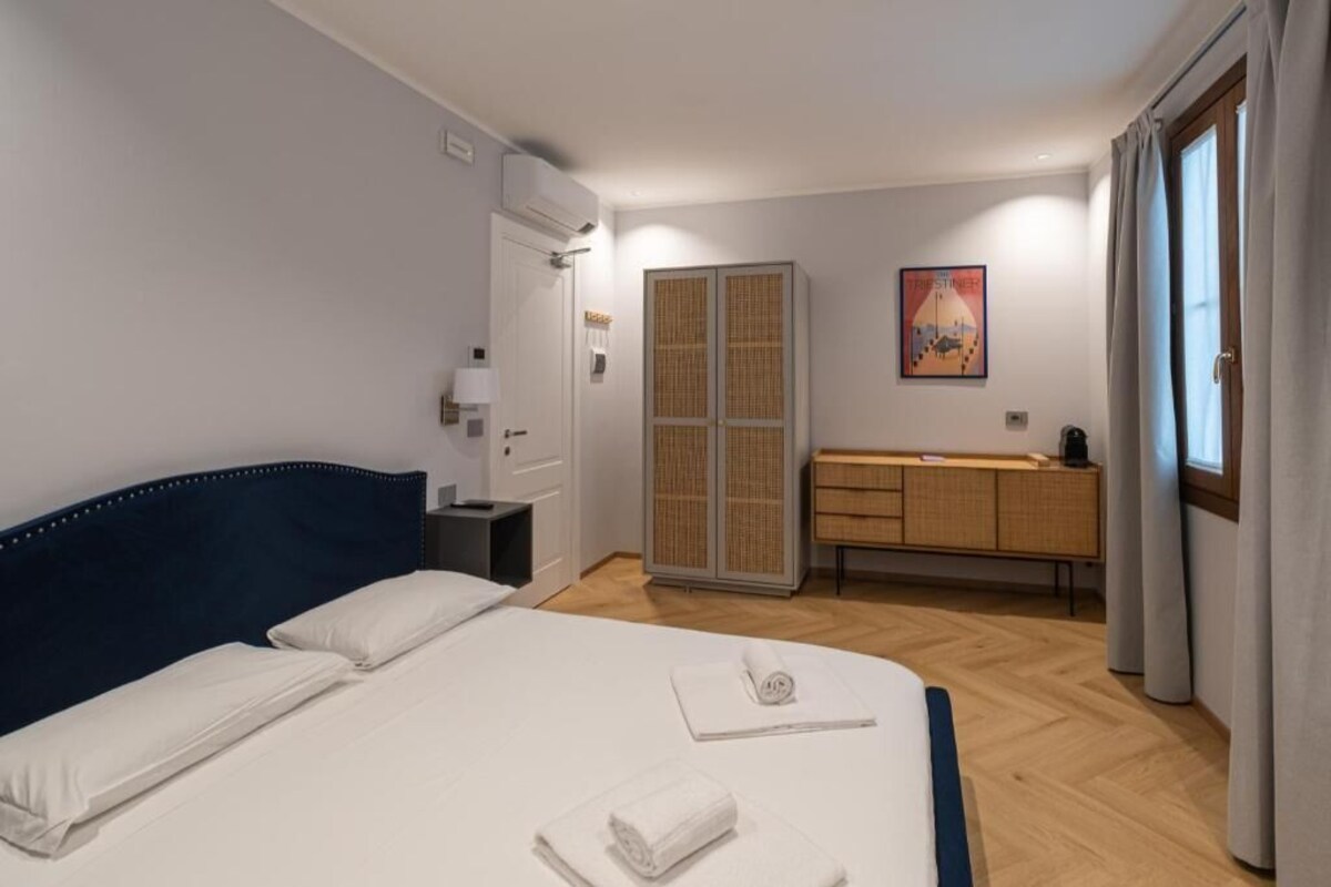 Ein Hotelzimmer mit Bett, Nachttisch, Kleiderschrank, Badezimmer und einem Fenster mit Vorhängen.