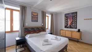 A hotel room with a bed, a nightstand, a wooden dresser, and a poster on the wall. - 23 SUITES (TRIESTE)
