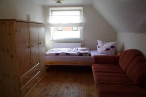 A small, single-bed room with a sloped ceiling, a wooden wardrobe, a window with blinds, and a red sofa. - Holiday home with 2 bedrooms (Waren\/Müritz)