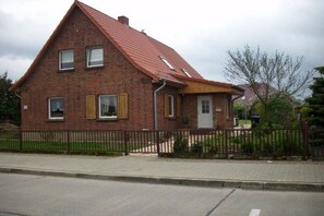 A two-story brick house with a red roof, a fenced yard, and a small front porch. - Holiday home with 2 bedrooms (Waren\/Müritz)