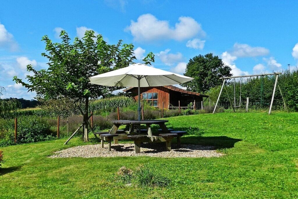 A picnic area with a table and benches, a swing set, and a building in the background.