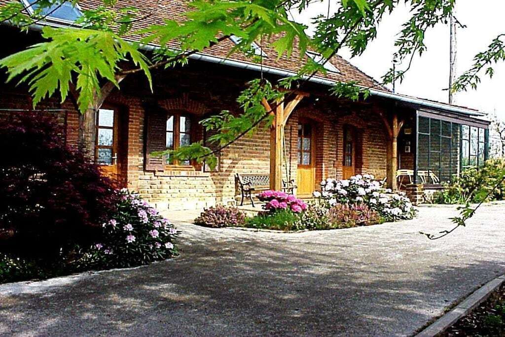 Un bâtiment en briques doté d’un porche, d’un banc et d’un jardin fleuri.
