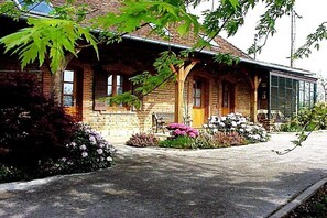 A brick building with a porch, a bench, and a garden with flowers. - Domaine du Val des Ragondins (Sainte Croix)