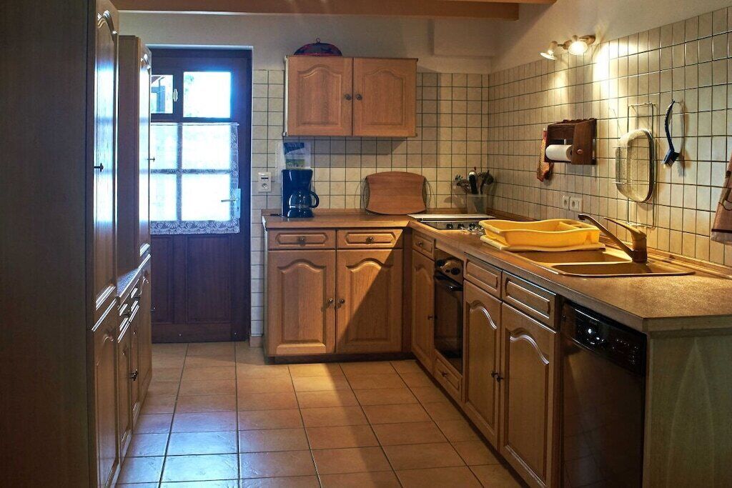 A kitchen with wooden cabinets, a dishwasher, and a window with blinds.
