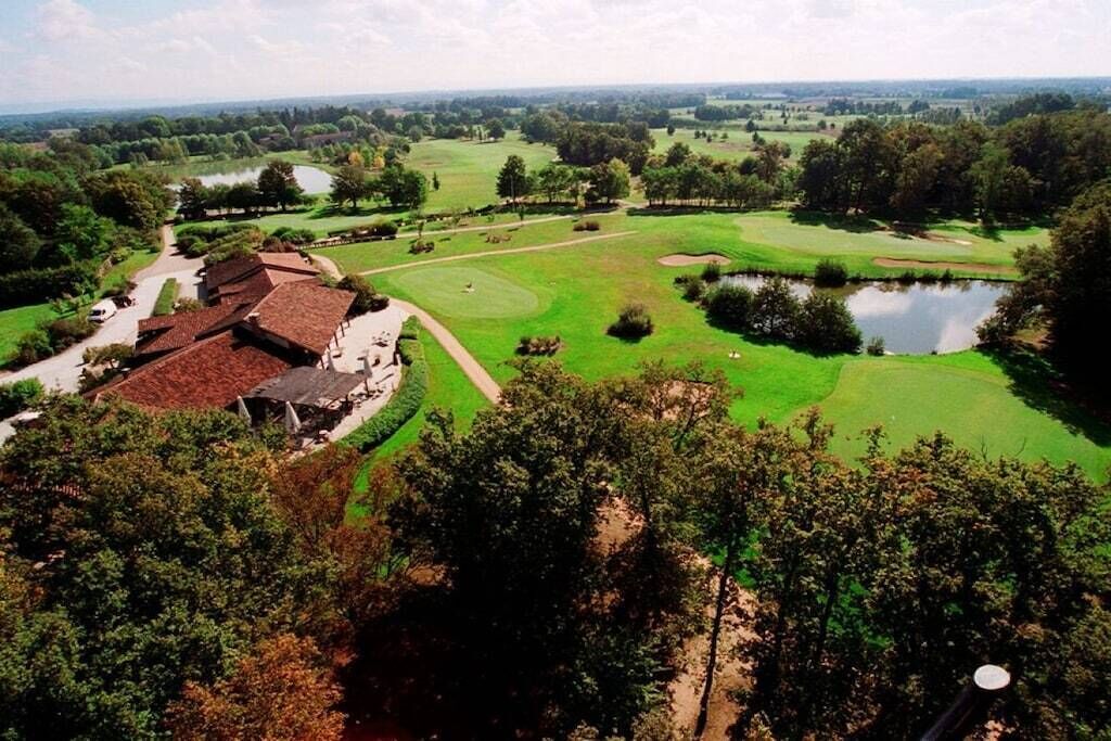 Ein Golfplatz mit Teich, umgeben von Bäumen und einem Gebäude mit rotem Dach.