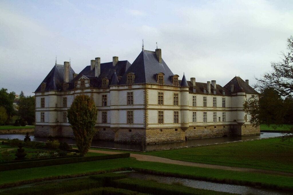 A large, historic building with multiple chimneys, a symmetrical facade, and a moat surrounding the property.