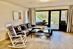 Un salon comprenant un canapé, un fauteuil à bascule, une table basse et une vue sur l’extérieur, visible à travers une porte vitrée.