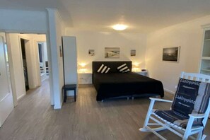A bedroom with a bed, bedside tables, a chair, and a door leading to another room. - Holiday apartment with 2 bedrooms (Hörnum)