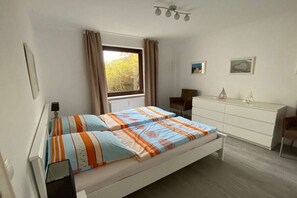 Een slaapkamer met een bed, een dressoir, een stoel en een raam met gordijnen.