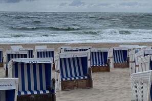 Strandstoelen met nummers, gerangschikt op een zandstrand met de oceaan op de achtergrond.