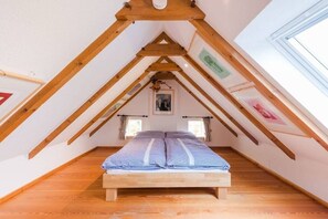 Ein Schlafzimmer mit schrägen Wänden, Holzbalken, einem Bett mit kariertem Überwurf und einem Fenster.