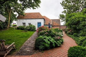 A white building with a red-tiled roof, a brick pathway, and lush greenery. - Holiday home with 2 bedrooms (Greetsiel)