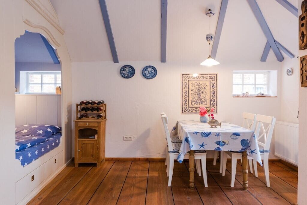 Una habitación con una cama, una mesa de comedor, sillas, un armario de madera y un tapiz con motivos.