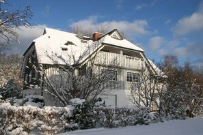 Een twee verdiepingen tellend huis met een sneeuwbedekte kap en schoorsteen.