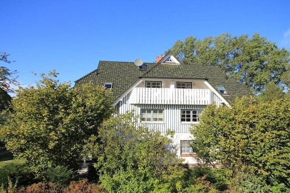 Een tweelaags huis met een puntige dakschildering, een witte gevel en een zichtbare schotelantenne.