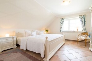 Een slaapkamer met een enkel bed, nachtkastjes, een raam met gordijnen, een radiator en een stoel.