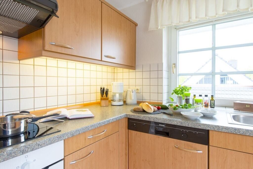 Una cocina con armarios de madera, lavavajillas, estufa y ventana con vista a edificios.