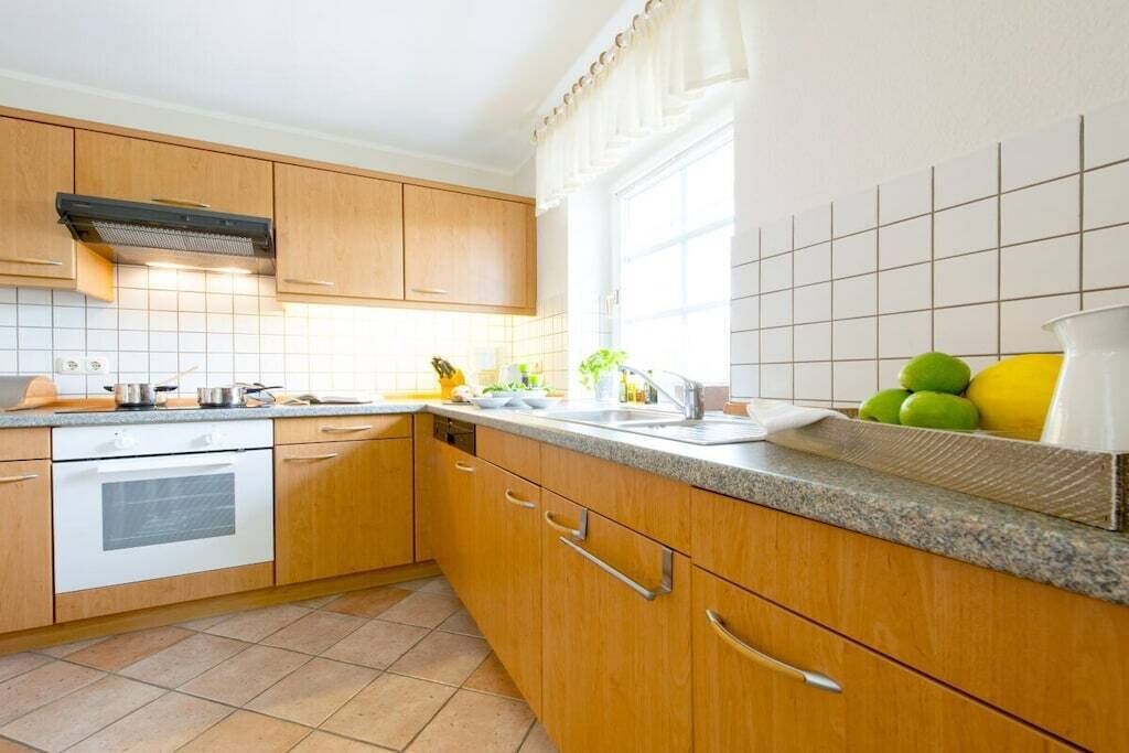 Una cocina con armarios de madera, un horno blanco, un fregadero y una ventana con cortinas.