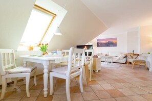 Een eethoek met een witte tafel en stoelen, een televisie en een schilderij aan de muur.