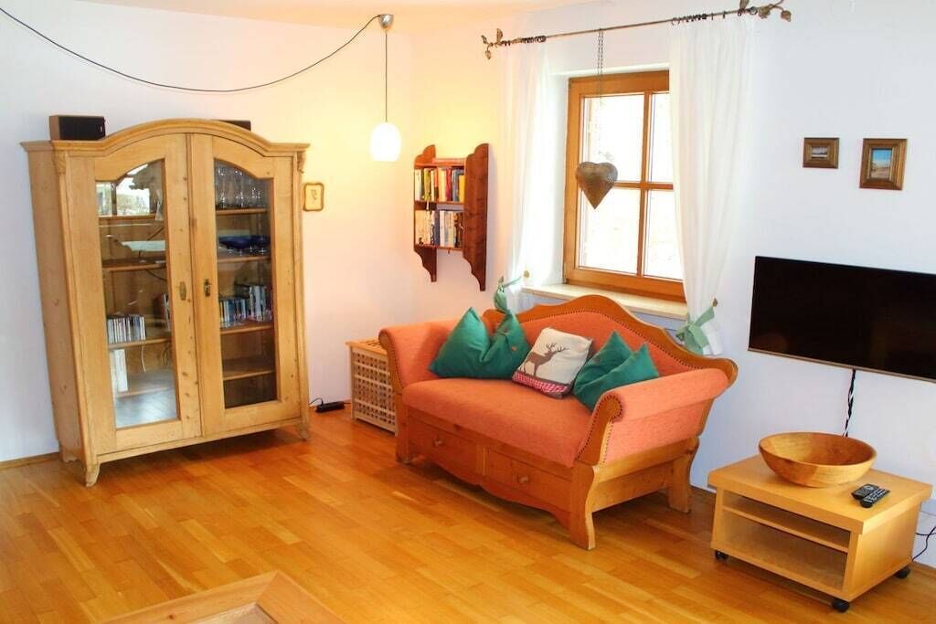 Ein möbliertes Wohnzimmer mit einer Couch, einem Holzschrank, einem Fernseher und einem Fenster mit Vorhängen.
