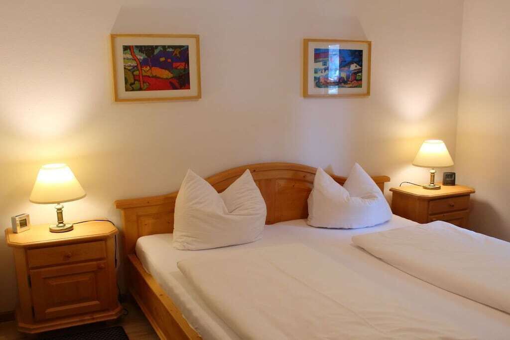 Quarto de hotel com cama de casal, duas mesas de cabeceira com abajures e duas obras de arte emolduradas na parede.