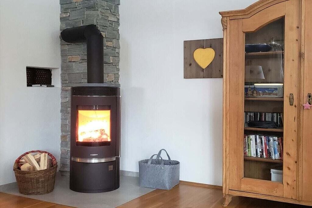 Ein Zimmer mit Kaminofen, Steinwand, Herzförmiger Dekoration, Holzschrank mit Büchern und einem Korb mit Holzscheiten.