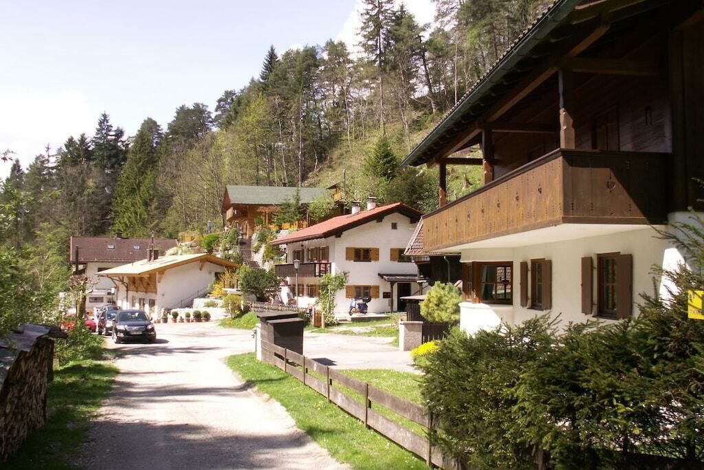 Eine Reihe traditioneller Holzhäuser mit geneigten Dächern, einer gepflasterten Auffahrt und einem bewaldeten Hang im Hintergrund.