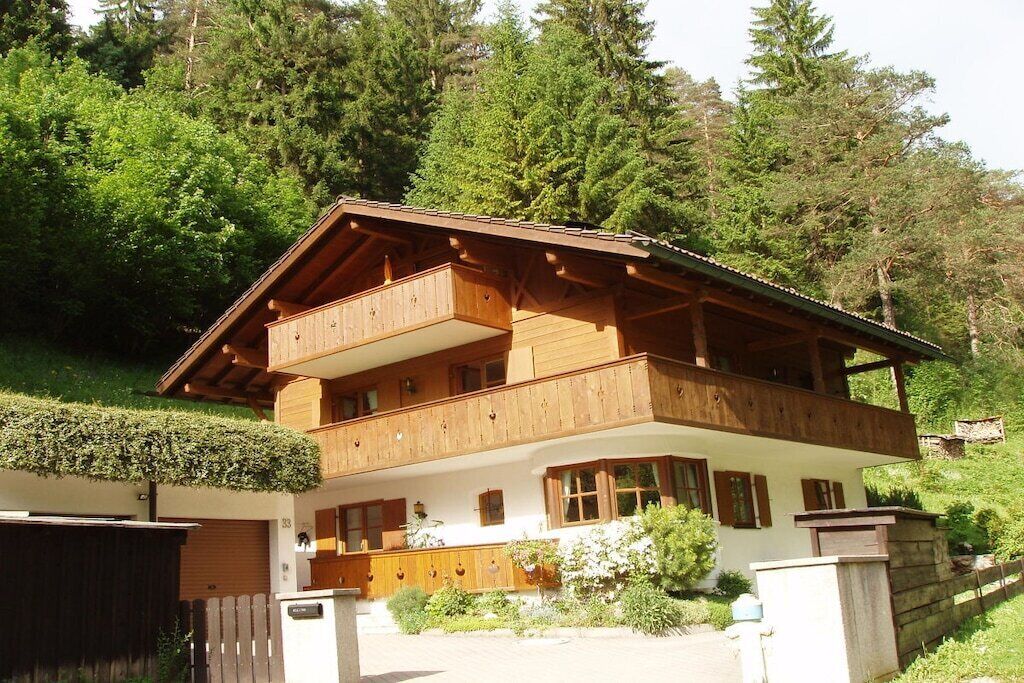 Een houten chalet met twee verdiepingen, inclusief een balkon op de bovenste etage, omringd door groen en bomen.