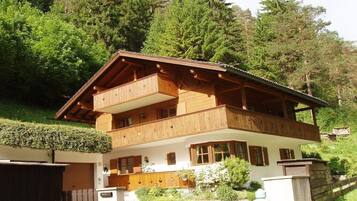 Een houten chalet met twee verdiepingen, inclusief een balkon op de bovenste etage, omringd door groen en bomen.