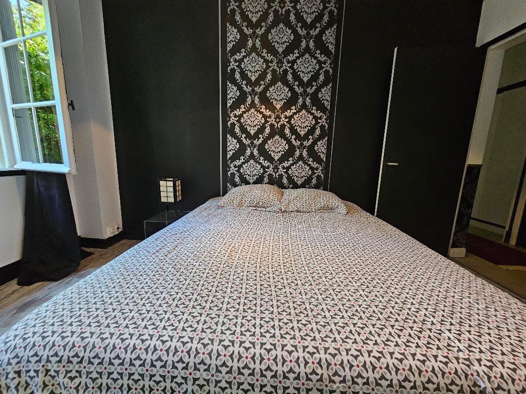 Un dormitorio con una colcha estampada, una ventana con cortinas y una pared decorada.
