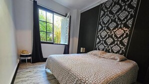 Una camera da letto con un letto, una finestra con tende, un tavolino e una parete decorata.