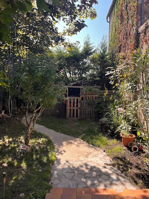 A garden pathway leading to a wooden structure, surrounded by various plants and a brick wall. - Charming house with a garden in Monpazier, the most beautiful bastide in the Périgord (Monpazier)