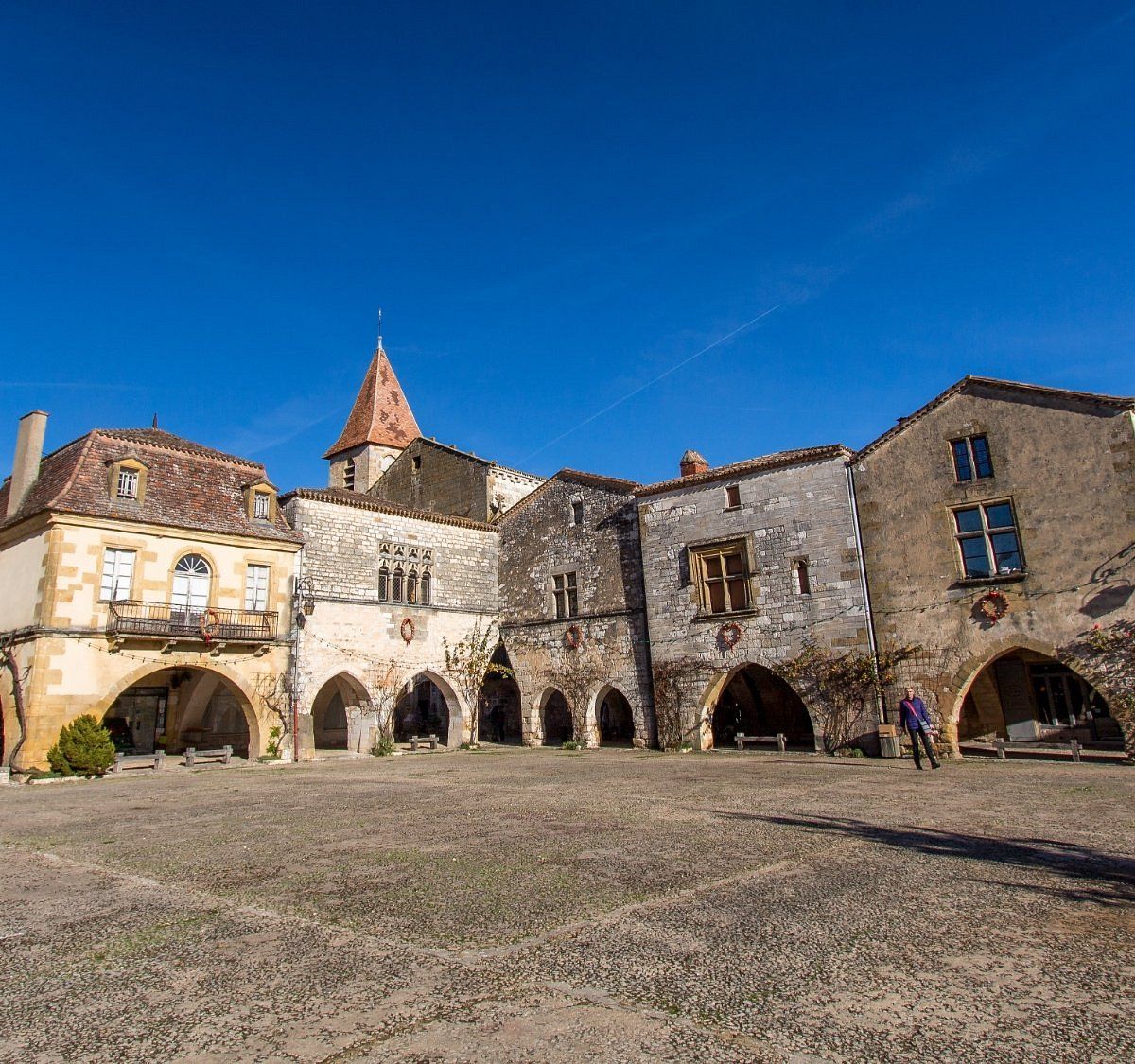 A courtyard with historic stone buildings, including a church with a pointed roof and arched walkways.