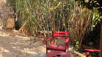 A red bench and table set in a garden with a stone wall and tall plants.