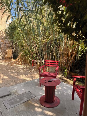 A red bench and table set in a garden with a stone wall and tall plants. - Charming house with a garden in Monpazier, the most beautiful bastide in the Périgord (Monpazier)