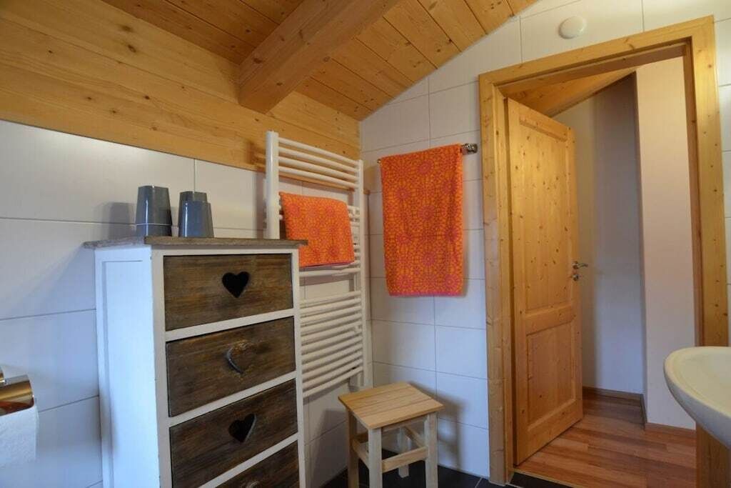 Een badkamer met houten lambrisering, een wit kastje, een houten kruk en een houten deur.