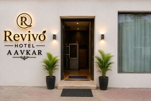 Exterior do Hotel Revivo Aavkar, com uma entrada moderna, duas plantas em vasos e uma grande janela.