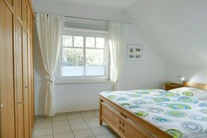 A bedroom with a bed, a window with curtains, a bedside table, and a wall-mounted light. - Holiday home in Prerow with swimming pool (Prerow)