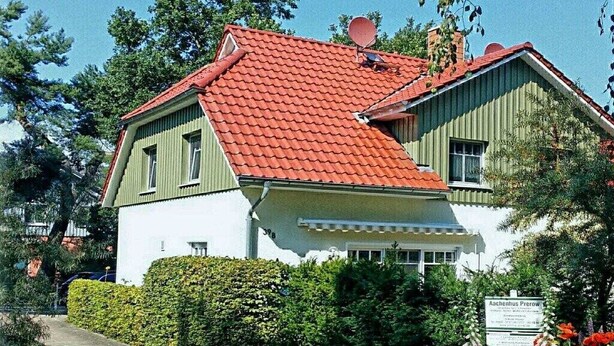 Une maison à deux étages, avec un toit recouvert de tuiles rouges, une façade verte et blanche, et une pancarte indiquant qu’il s’agit d’une résidence privée.