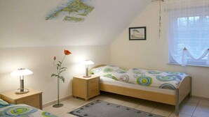 Une chambre avec un lit simple, deux tables de chevet, une lampe, une carte accrochée au mur et une fenêtre avec des rideaux.