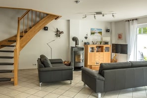 A living room with a wooden staircase, two sofas, a fireplace, and a television. - Holiday home in Prerow with swimming pool (Prerow)