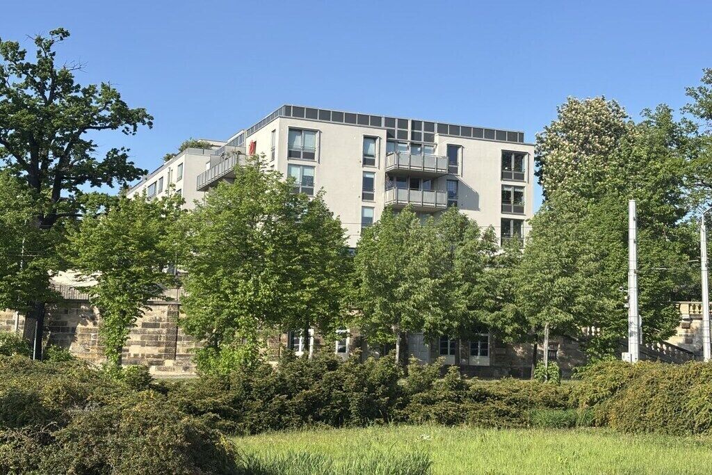 A multi-story building with a flat roof, surrounded by trees and greenery.