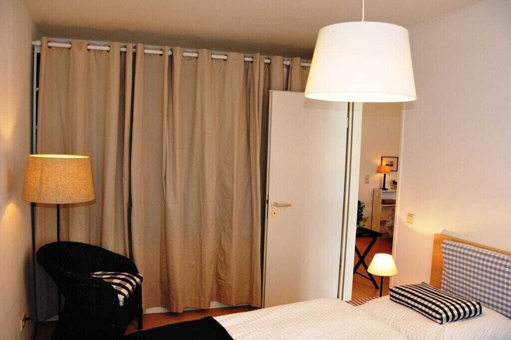 A hotel room with a bed, a chair, a lamp, and a curtain.