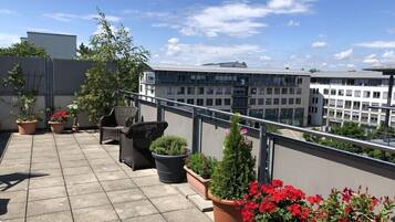 A rooftop terrace with potted plants, outdoor furniture, and a view of surrounding buildings.