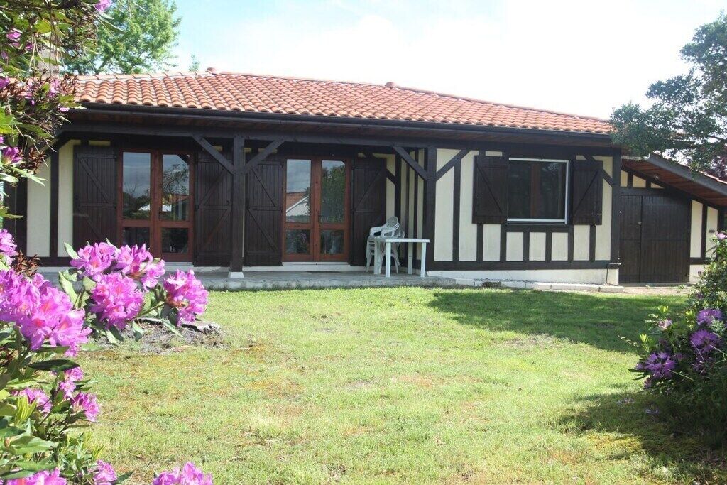 A two-story building with a tiled roof, large windows, and a small patio area with a table and chairs.