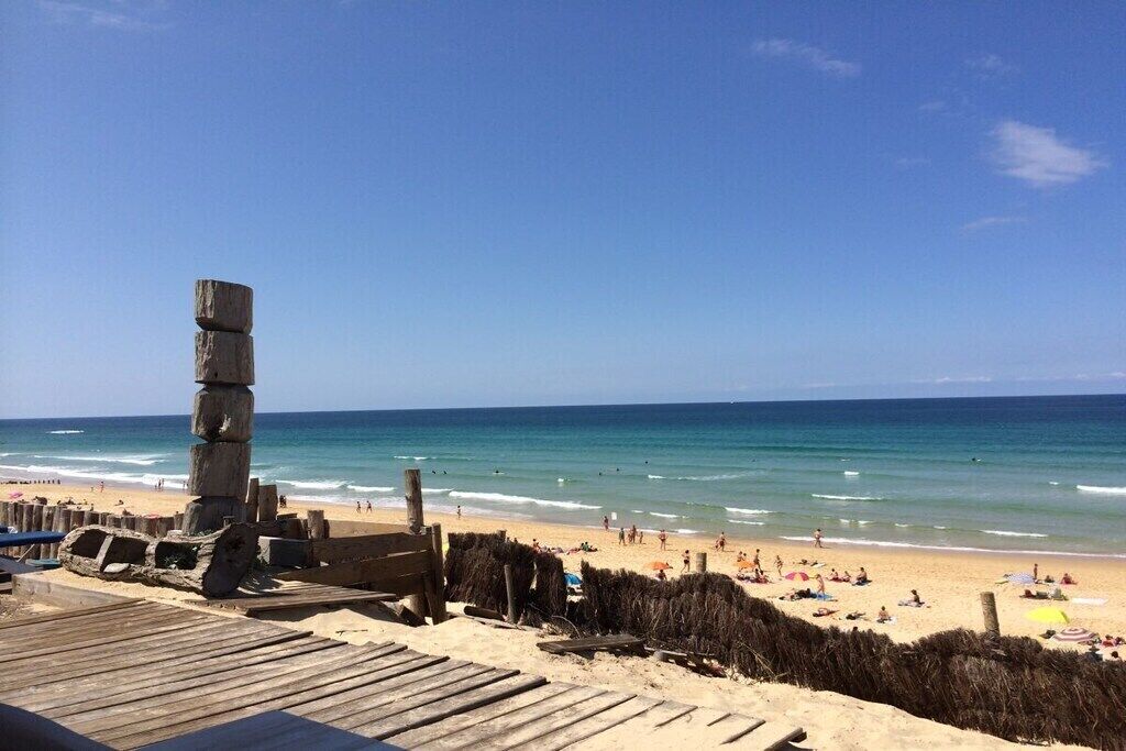 A beach with a wooden boardwalk, a stone structure, and people enjoying the seaside.