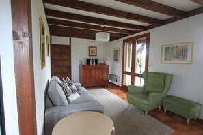 Ein Wohnzimmer mit einer Couch, einem grünen Sessel, einer Holzkommode und einem runden Tisch.