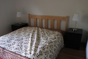 Ein Einzelbett mit Holz-Kopfteil, zwei Nachttische mit Lampen und eine zart gemusterte Bettdecke.